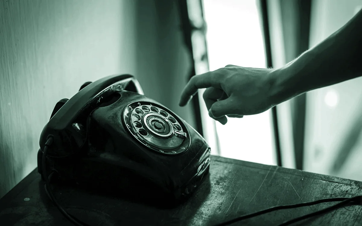 Una mano alcanzando un teléfono de disco sobre una mesa